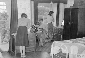 Enjoying a quiet spot on a bench under the trees in the garden of the rest break house in Torquay are (left to right) Mrs Eivemark (the forewoman of a WLA hostel), Miss Mary Pakes, Miss Ann Royne (WLA gang work forewoman) and Mrs Joan Hart (timber corps crane driver). Mrs Eivemark and Miss Pakes are chatting whilst Miss Royne and Miss Hart are reading a book together.